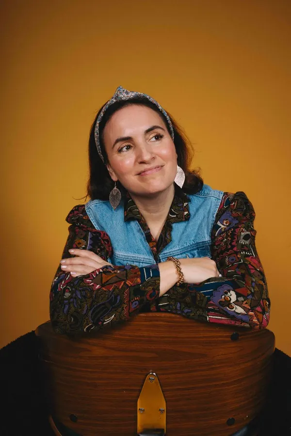 Talia smiling, in a patterned headband, against a warm orange backdrop